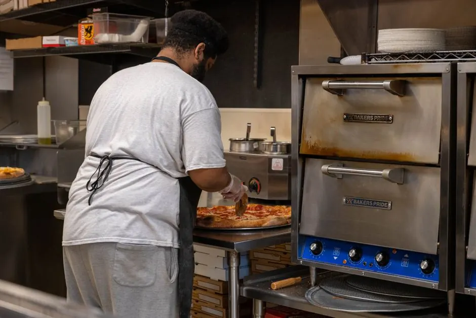 Chef slicing a freshly baked pizza in a commercial kitchen setting.